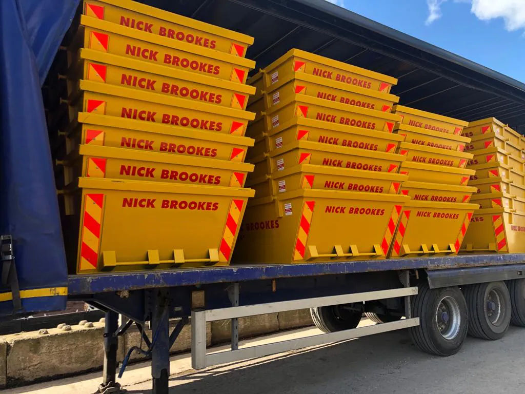 A lorry loaded with multiple bright yellow skips branded “Nick Brookes”, neatly stacked and ready for delivery at a yard.
